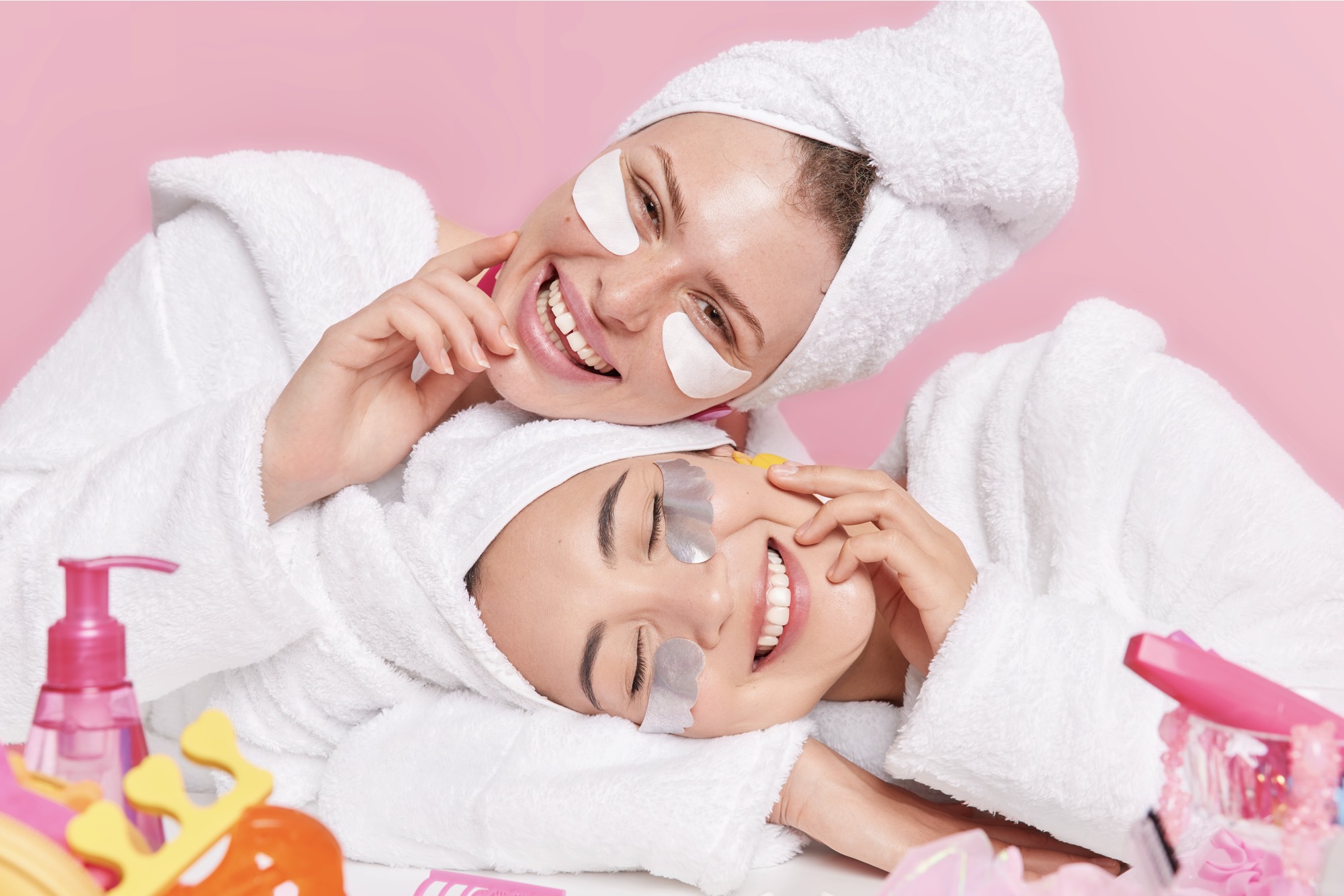 female models-smile-gladfully-tilt-heads-apply-beauty-patches-eyes-enjoys-skin-care-procedures-dressed-white-soft-bathrobes-isolated-pink